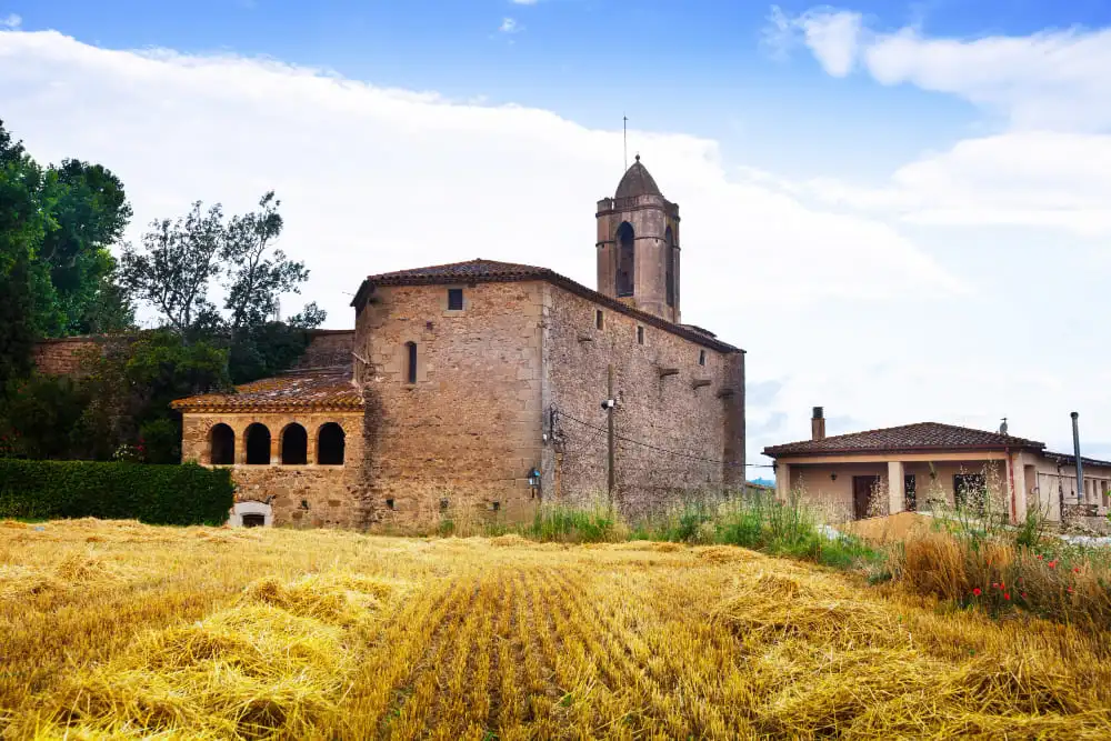 Projecte de restauració d'una antiga església de pedra i masia rústica a Catalunya envoltades d'un camp de blat segat. - Equip Cairat Reformes