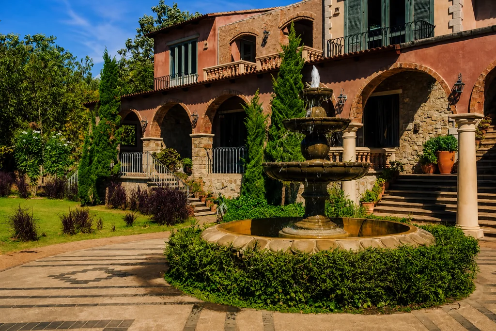 Façana exterior rústica d'una masia o granja antiga a Catalunya amb bigues de fusta, envoltada de camps verds i natura sota un cel assolellat. - Equip Cairat Reformes
